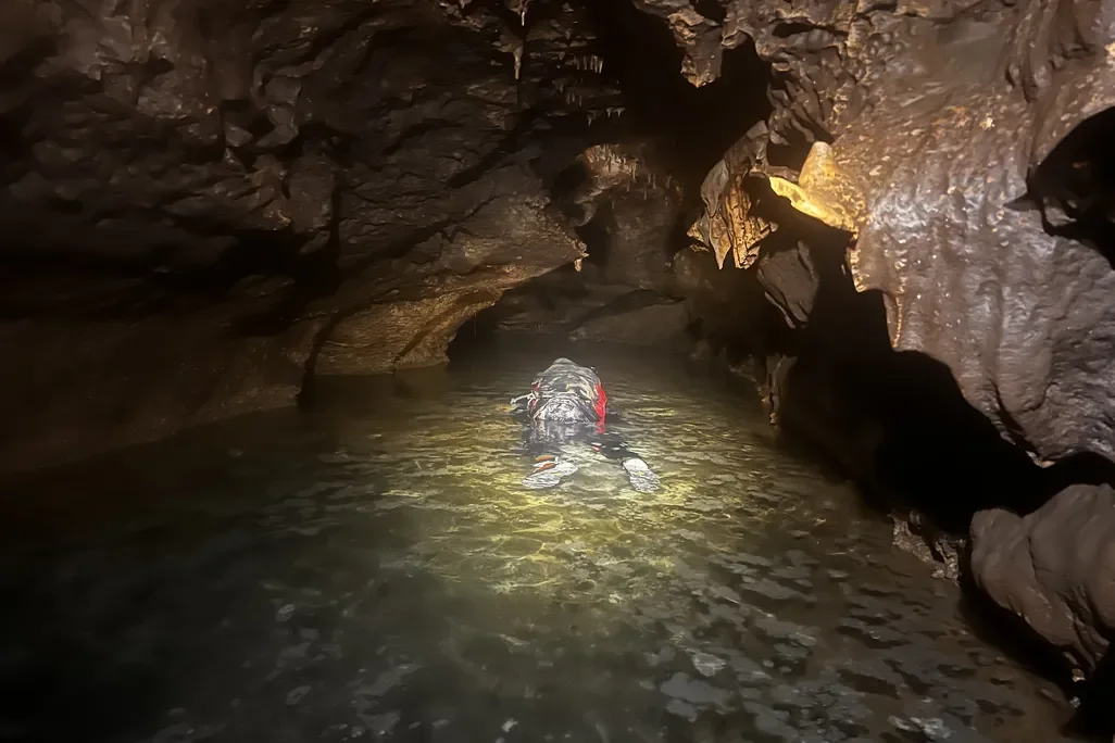 A person wearing a wetsuit in a stream in a cave